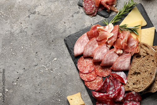 Slate plates with assortment of tasty deli meats, bread and cheese on grey background photo