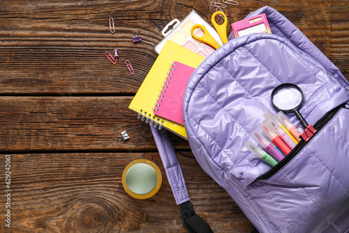 Lilac school backpack with bottle of juice and different stationery on wooden background