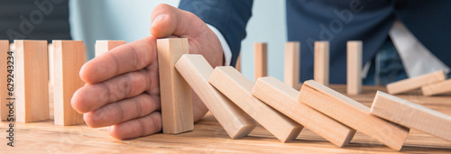 Tableau sur toile Businessman hand stopping falling wooden dominoes