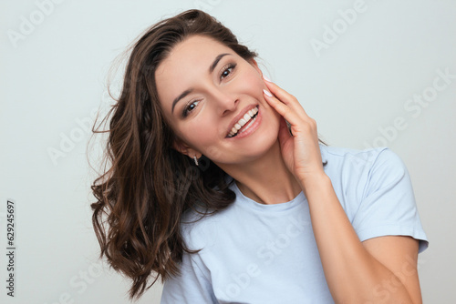 Konstfotografi a photo of a positive young dark-haired Caucasian woman in a blue T-shirt, who smiling and touching her face with her hand
