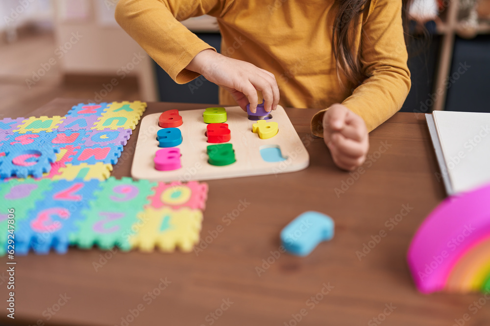 Adorable hispanic girl playing with maths puzzle game sitting on table at kindergarten Adorable hispanic girl playing with maths puzzle game sitting on table at kindergarten