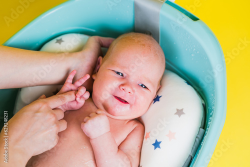 A newborn baby takes a bath on a yellow background. A lovely child is undergoing military training for the first time. The concept of children and hygiene