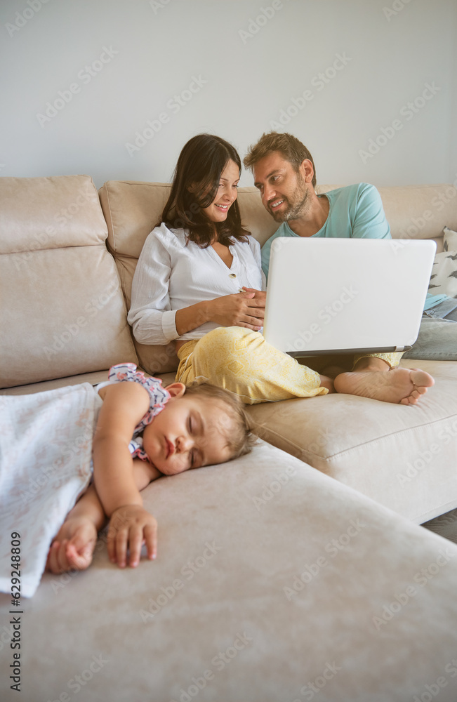 Mother and father browsing laptop near sleeping daughter