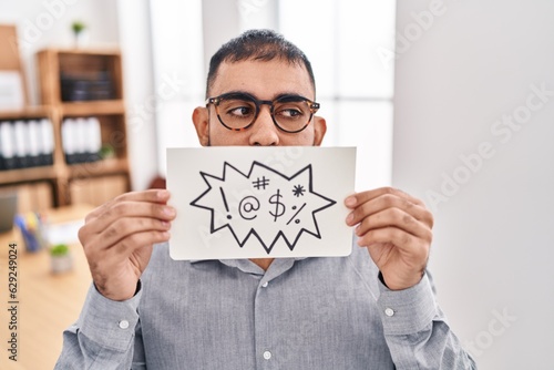 Middle east man with beard holding banner with swear words smiling looking to the side and staring away thinking.