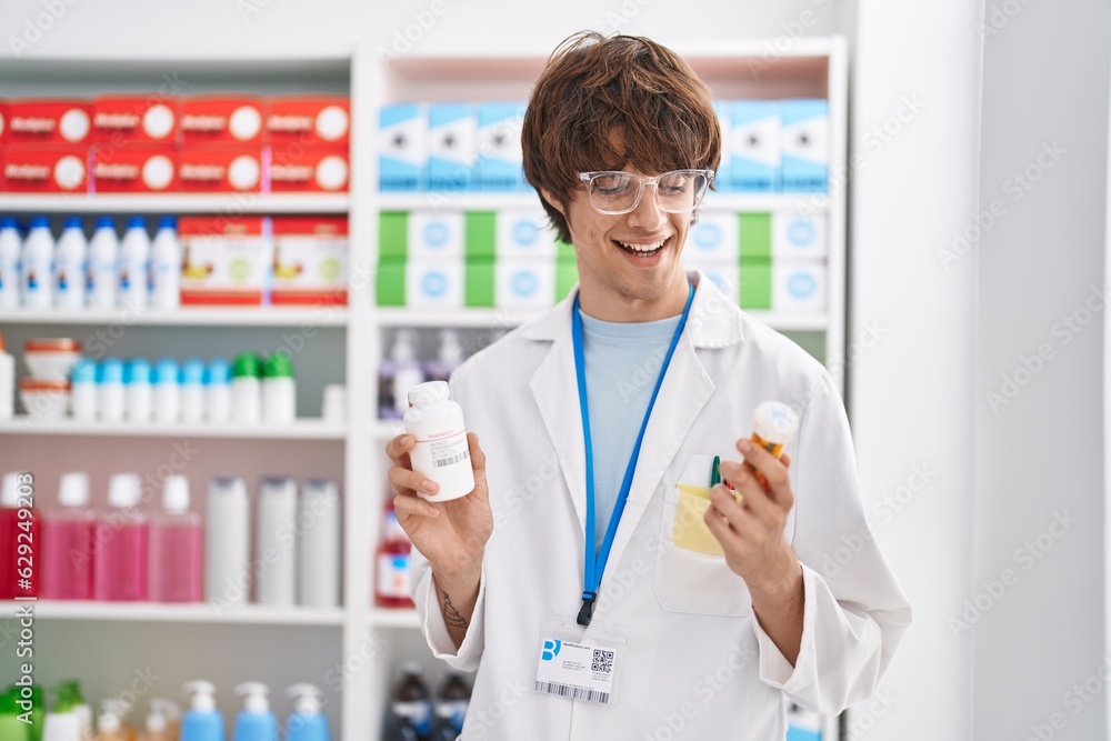 Young blond man pharmacist smiling confident holding pills bottles at pharmacy