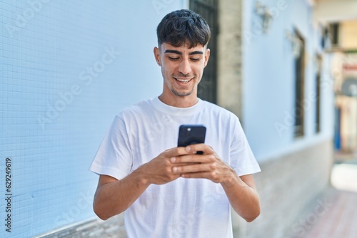 Young hispanic man smiling confident using smartphone at street