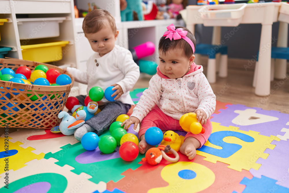 Adorable boy and girl playing with balls sitting on floor at kindergarten Adorable boy and girl playing with balls sitting on floor at kindergarten