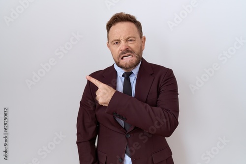 Middle age business man with beard wearing suit and tie pointing aside worried and nervous with forefinger, concerned and surprised expression