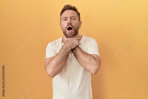 Middle age man with beard standing over yellow background shouting suffocate because painful strangle. health problem. asphyxiate and suicide concept.