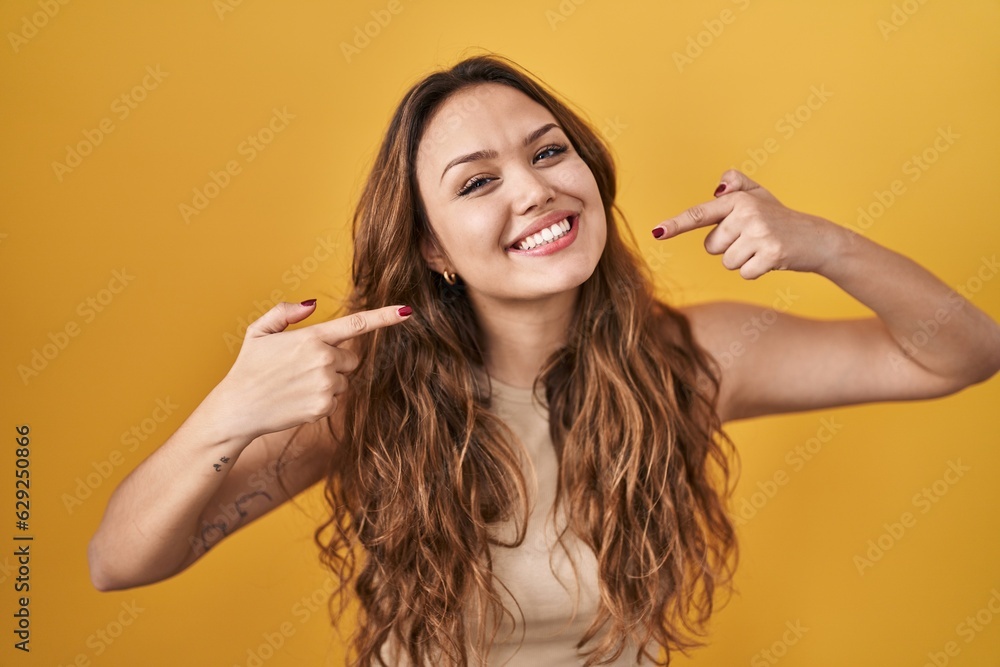 Young hispanic woman standing over yellow background smiling cheerful showing and pointing with fingers teeth and mouth. dental health concept. Young hispanic woman standing over yellow background smiling cheerful showing and pointing with fingers teeth and mouth. dental health concept.