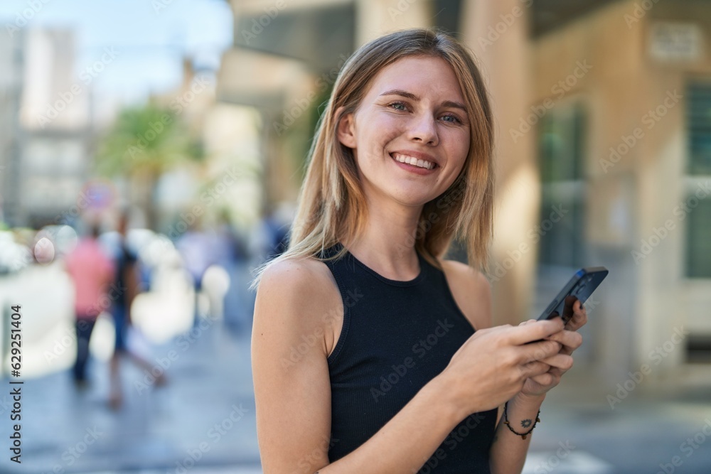 Young blonde woman using smartphone smiling at street Young blonde woman using smartphone smiling at street