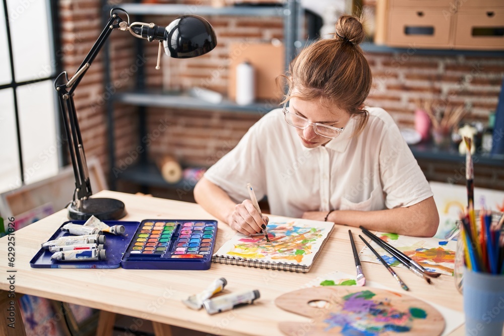 Young blonde woman drawing on notebook at art studio