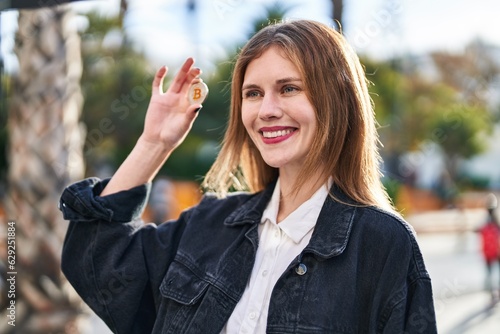 Young blonde woman holding bitcoin smiling at street