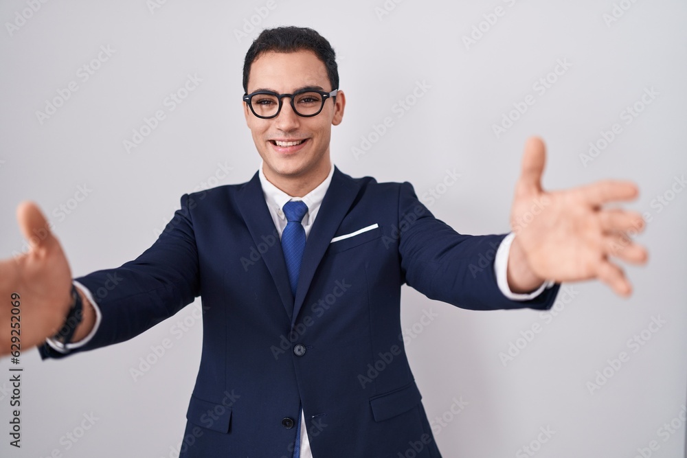 Young hispanic man wearing suit and tie looking at the camera smiling with open arms for hug. cheerful expression embracing happiness. Young hispanic man wearing suit and tie looking at the camera smiling with open arms for hug. cheerful expression embracing happiness.