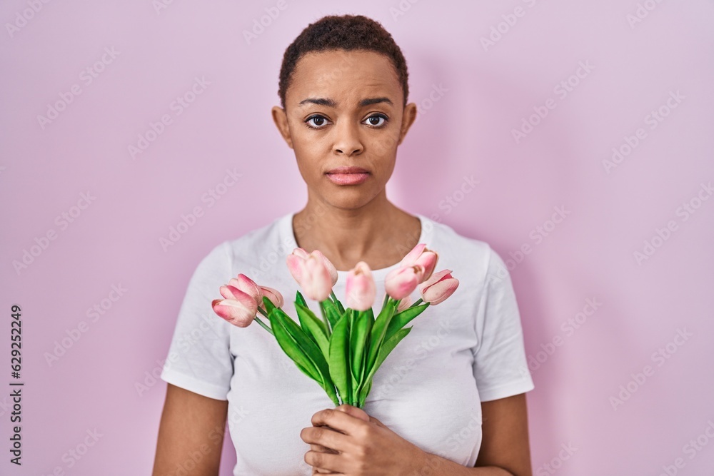 Beautiful african american woman holding bouquet of pink tulips flowers relaxed with serious expression on face. simple and natural looking at the camera. Beautiful african american woman holding bouquet of pink tulips flowers relaxed with serious expression on face. simple and natural looking at the camera.