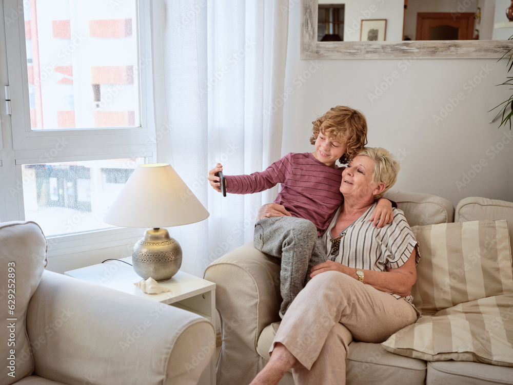 Aged woman on sofa with grandson using smartphone together Aged woman on sofa with grandson using smartphone together