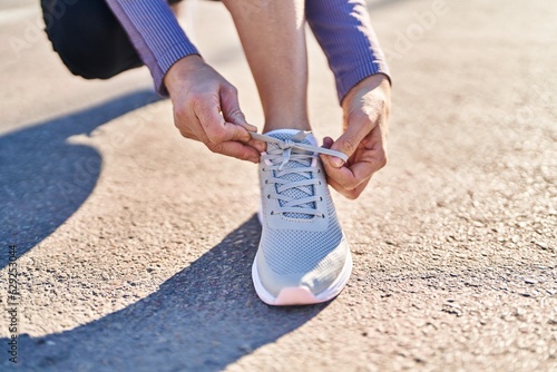 Young beautiful hispanic woman wearing sportswear tying shoe at street