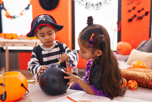 Adorable boy and girl having halloween party drawing on balloon at home