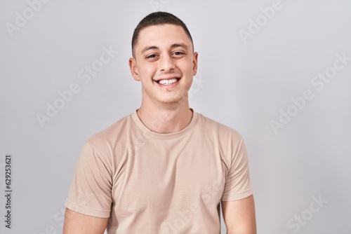 Young man standing over isolated background with hands together and crossed fingers smiling relaxed and cheerful. success and optimistic © Krakenimages.com