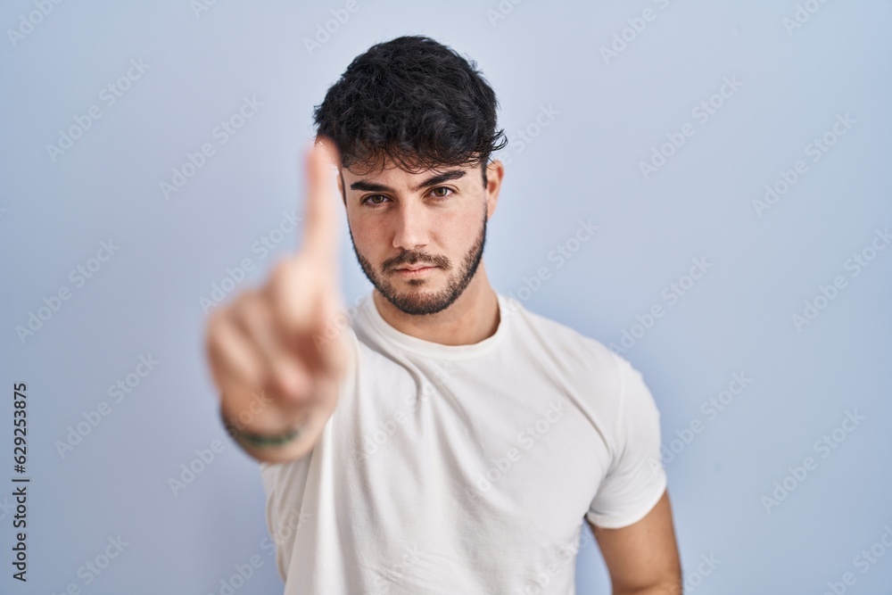 Hispanic man with beard standing over white background pointing with finger up and angry expression, showing no gesture Hispanic man with beard standing over white background pointing with finger up and angry expression, showing no gesture
