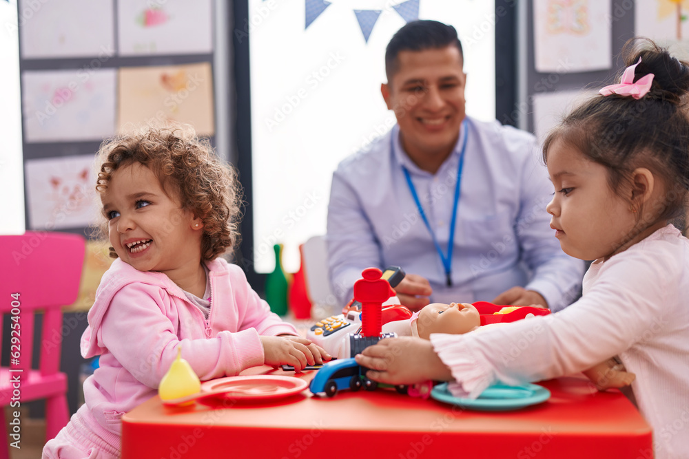 Hispanic man and girls playing supermarket game sitting on table at kindergarten Hispanic man and girls playing supermarket game sitting on table at kindergarten