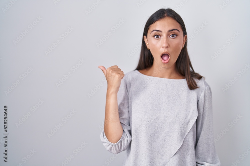 Young hispanic woman standing over white background surprised pointing with hand finger to the side, open mouth amazed expression. Young hispanic woman standing over white background surprised pointing with hand finger to the side, open mouth amazed expression.