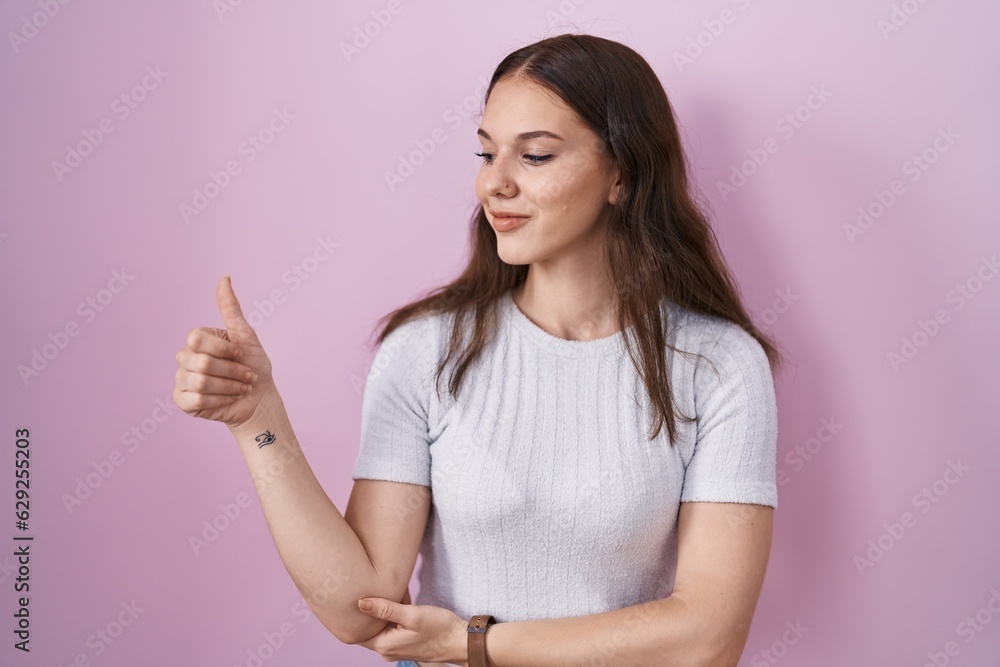 Young hispanic girl standing over pink background looking proud, smiling doing thumbs up gesture to the side Young hispanic girl standing over pink background looking proud, smiling doing thumbs up gesture to the side