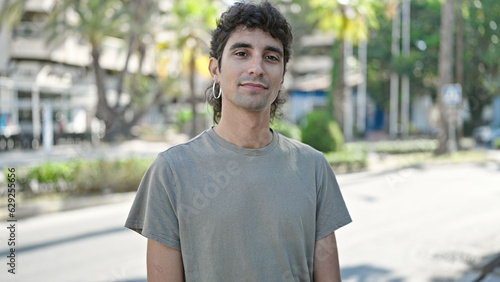 Young hispanic man standing with serious expression at street