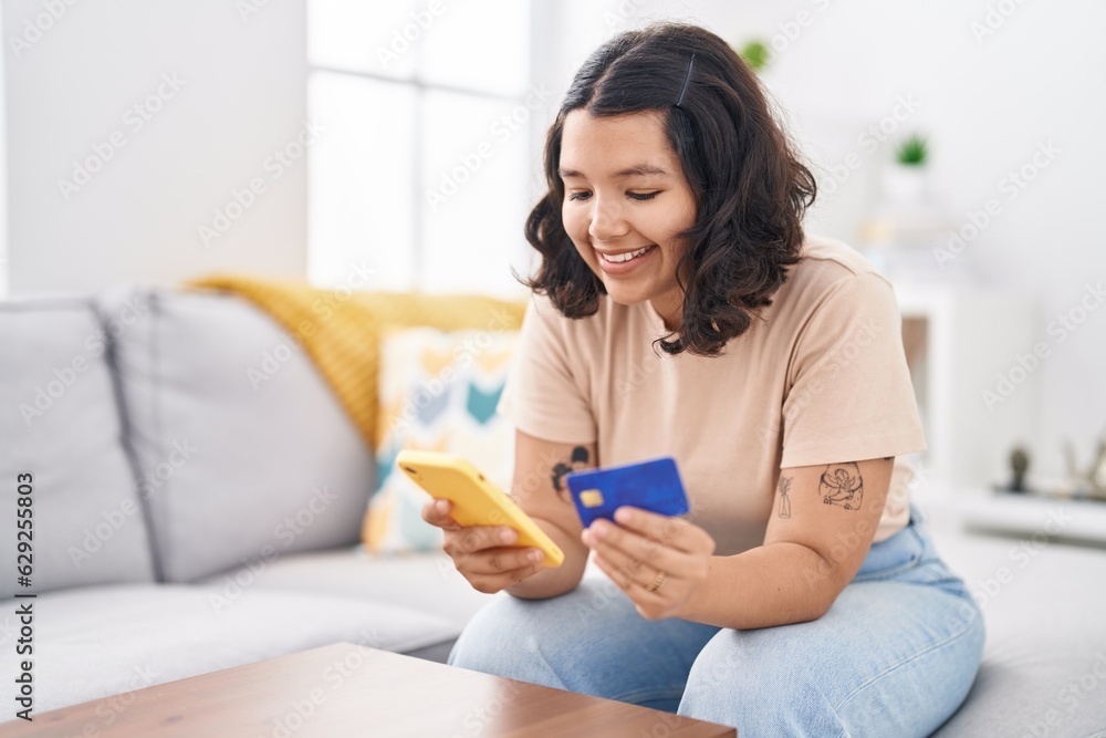 Young woman using smartphone and credit card sitting on sofa at home Young woman using smartphone and credit card sitting on sofa at home