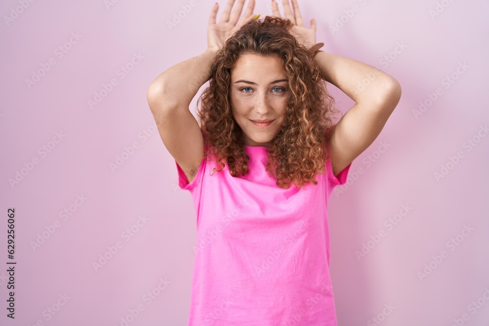 Young caucasian woman standing over pink background doing bunny ears gesture with hands palms looking cynical and skeptical. easter rabbit concept.