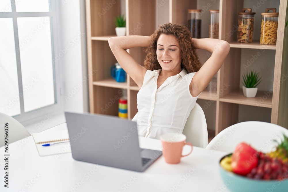 Young beautiful hispanic woman using laptop relaxed with hands on head at home
