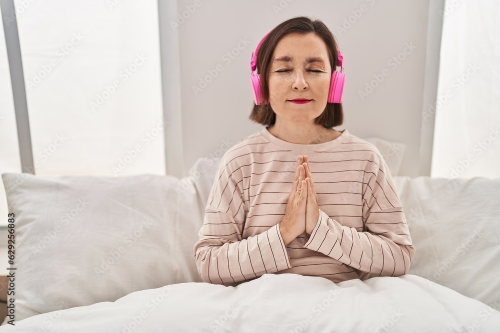 Middle age woman doing yoga exercise sitting on bed at bedroom