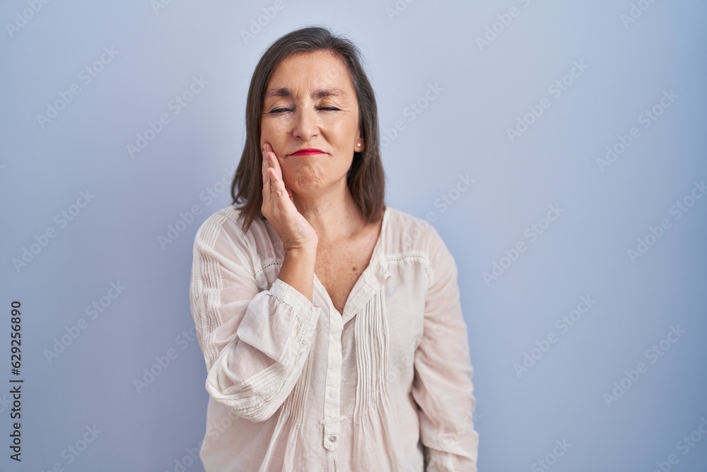 Middle age hispanic woman standing over blue background touching mouth with hand with painful expression because of toothache or dental illness on teeth. dentist Middle age hispanic woman standing over blue background touching mouth with hand with painful expression because of toothache or dental illness on teeth. dentist