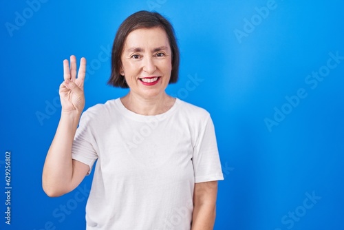 Wallpaper Mural Middle age hispanic woman standing over blue background showing and pointing up with fingers number three while smiling confident and happy. Torontodigital.ca