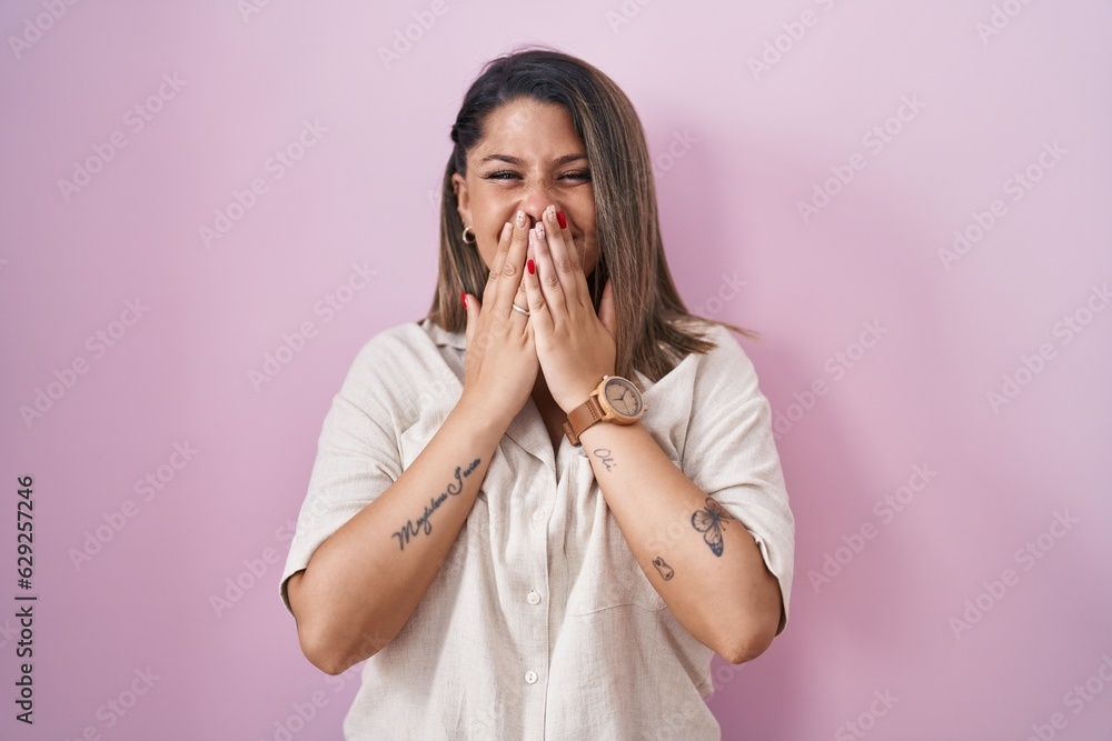 Blonde woman standing over pink background laughing and embarrassed giggle covering mouth with hands, gossip and scandal concept Blonde woman standing over pink background laughing and embarrassed giggle covering mouth with hands, gossip and scandal concept