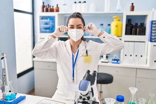 Young beautiful hispanic woman scientist smiling confident wearing medical mask at laboratory