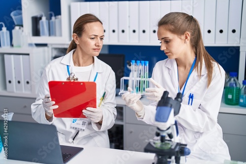 Two women scientists write on document holding test tubes at laboratory