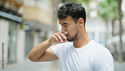 Young hispanic man sneezing at street
