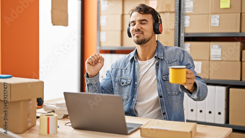 Young hispanic man ecommerce business worker listening to music drinking coffee at office