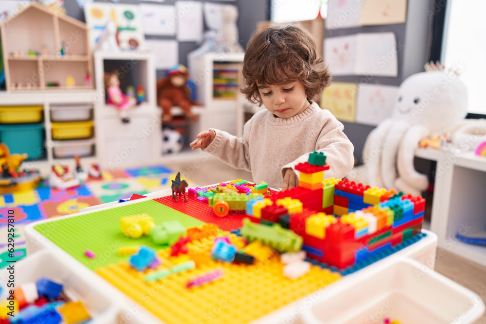Fototapeta premium Adorable hispanic boy playing with construction blocks standing at kindergarten