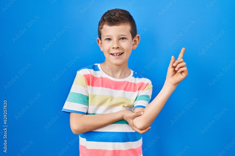 Young caucasian kid standing over blue background with a big smile on face, pointing with hand finger to the side looking at the camera. Young caucasian kid standing over blue background with a big smile on face, pointing with hand finger to the side looking at the camera.