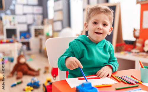 Adorable caucasian boy preschool student sitting on table drawing on notebook at kindergarten