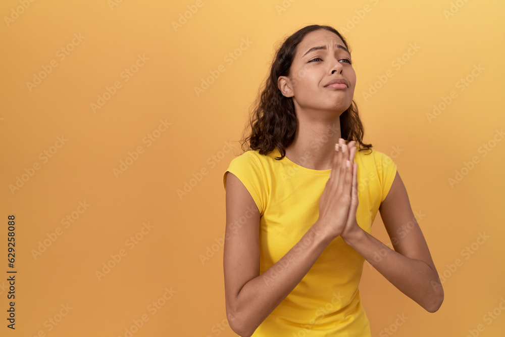 Young african american woman doing excuse gesture with hands together over isolated yellow background Young african american woman doing excuse gesture with hands together over isolated yellow background