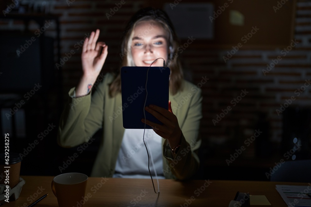 Blonde caucasian woman working at the office at night smiling positive doing ok sign with hand and fingers. successful expression.