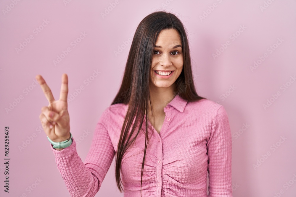 Young hispanic woman standing over pink background showing and pointing up with fingers number two while smiling confident and happy. Young hispanic woman standing over pink background showing and pointing up with fingers number two while smiling confident and happy.