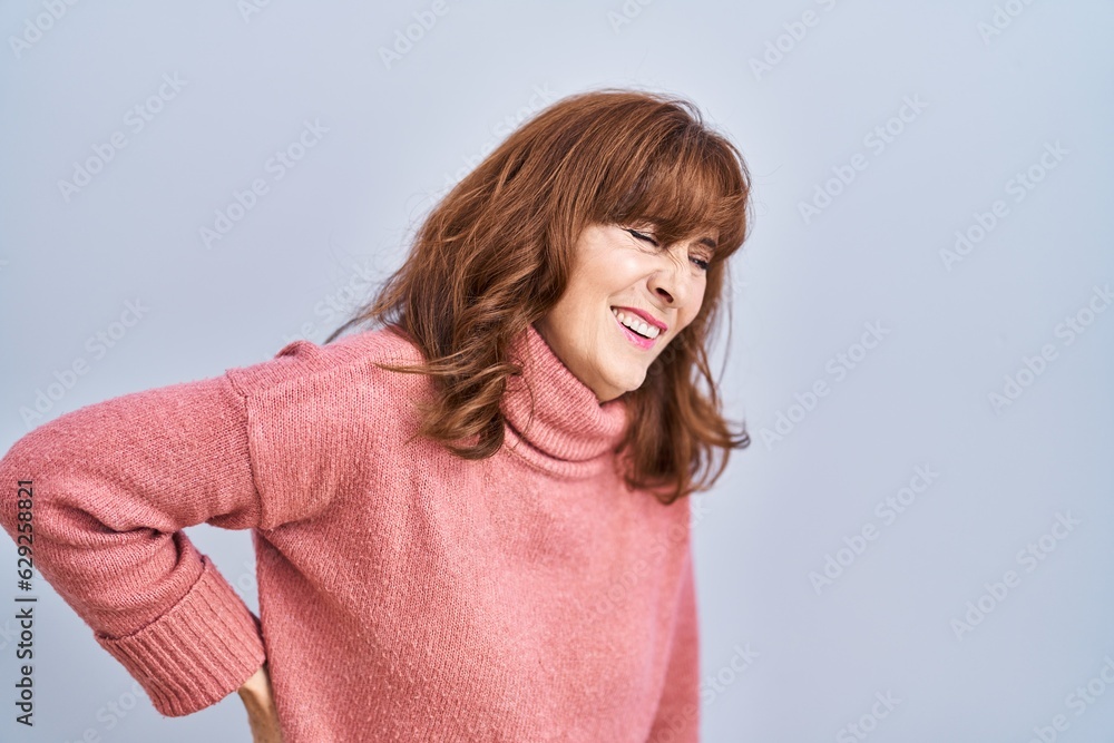 Middle age hispanic woman standing over isolated background suffering of backache, touching back with hand, muscular pain Middle age hispanic woman standing over isolated background suffering of backache, touching back with hand, muscular pain
