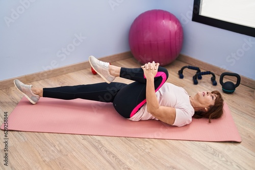 Middle age woman stretching leg at sport center