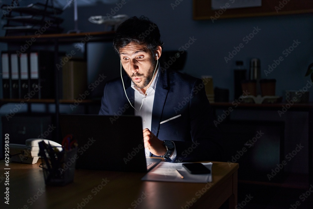 Handsome latin man working at the office at night scared and amazed with open mouth for surprise, disbelief face Handsome latin man working at the office at night scared and amazed with open mouth for surprise, disbelief face