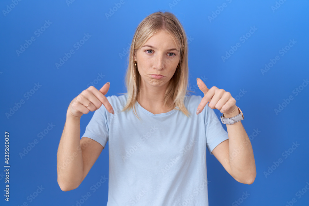 Young caucasian woman wearing casual blue t shirt pointing down looking sad and upset, indicating direction with fingers, unhappy and depressed. Young caucasian woman wearing casual blue t shirt pointing down looking sad and upset, indicating direction with fingers, unhappy and depressed.