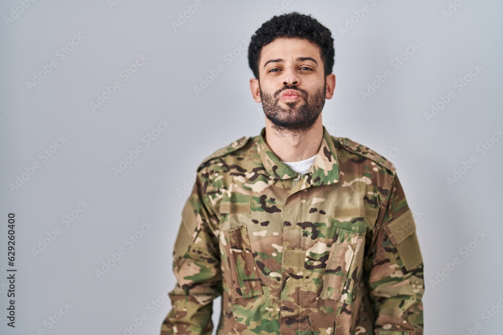 Arab man wearing camouflage army uniform looking at the camera blowing a kiss on air being lovely and sexy. love expression.